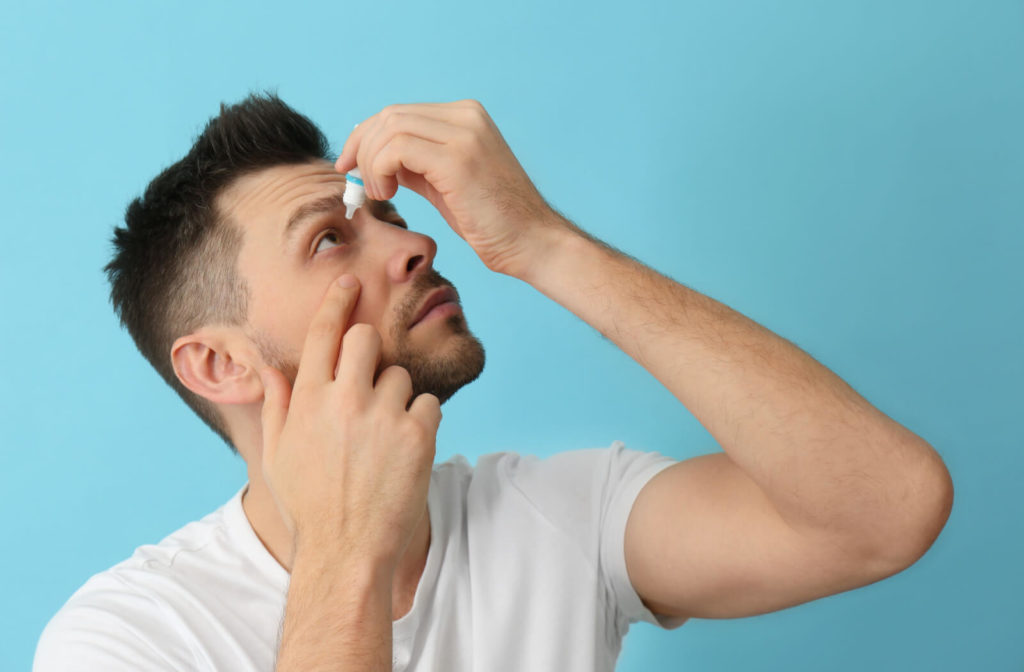 A man holding a small bottle of eye drops in his left hand and putting them on his right eye due to dry eyes.