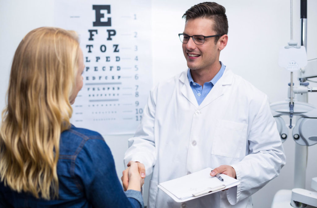 A woman in a medical exam room shaking hands with her optometrist.