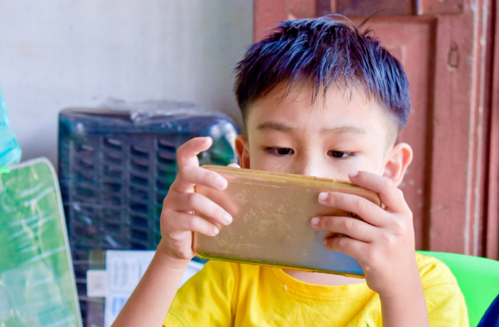 A child sitting on a chair and holding his smartphone very close to his face