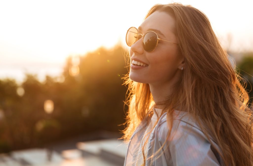 A close-up image of a woman smiling while wearing a pair of protective sunglasses outside.