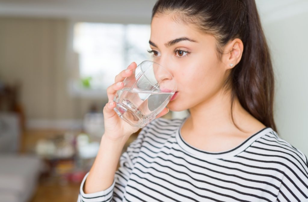 A woman at home drinks a glass of water to stay hydrated.