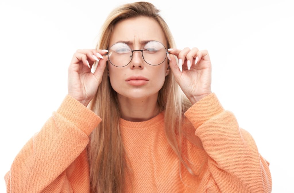A woman squints at the camera and adjusts the arms of her glasses