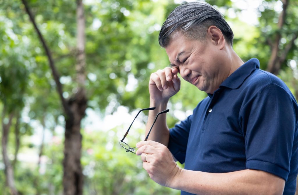 A man outdoors rubs his eye due to frustration from eye floaters