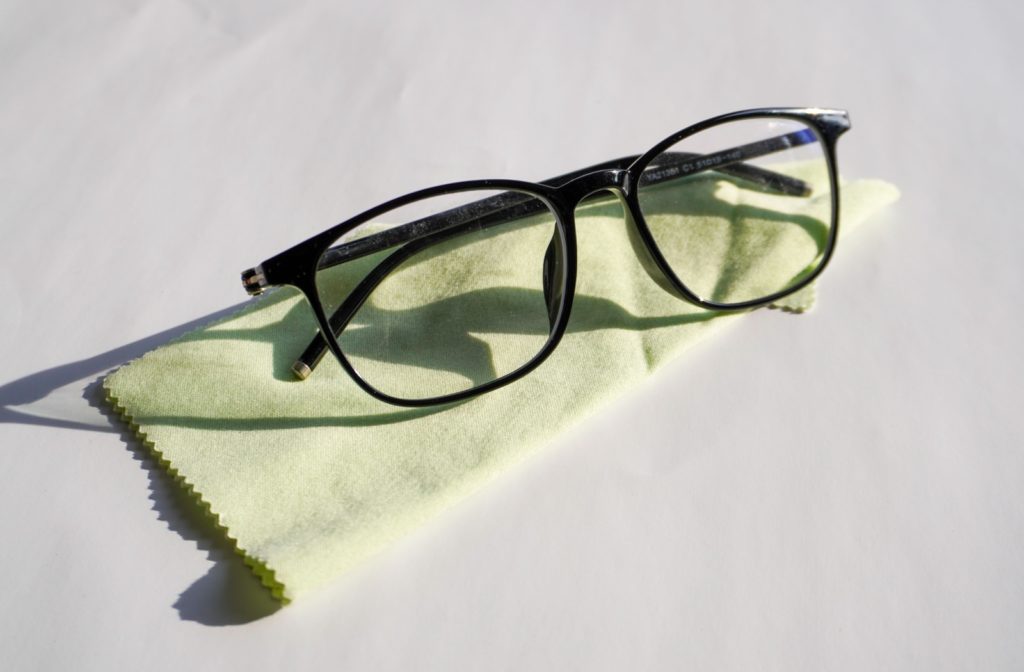 A pair of black plastic glasses sitting on top of a mint green microfiber cloth against a white background.