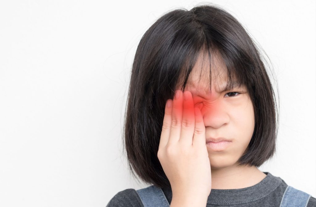 A child with pink eye winces and covers their infected eye.