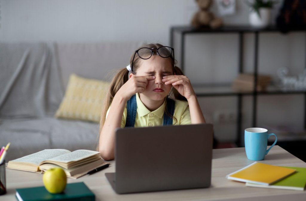 A child working on homework touches their eyes, risking spreading their pink eye.