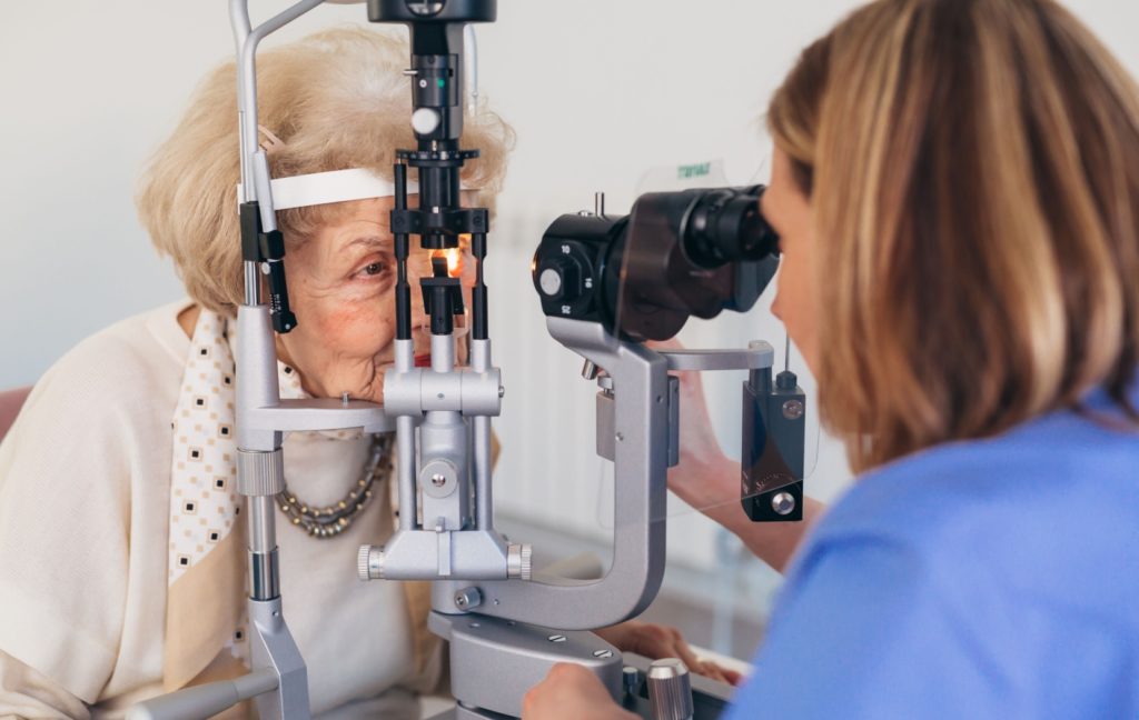 An optometrist uses a slit lamp to examine their senior patient's eyes to check for macular degeneration.