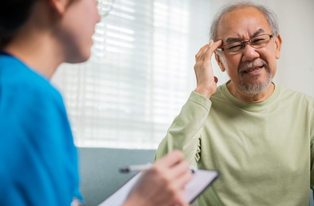 An older adult discussing their headache and blurry vision symptoms with an eye doctor.