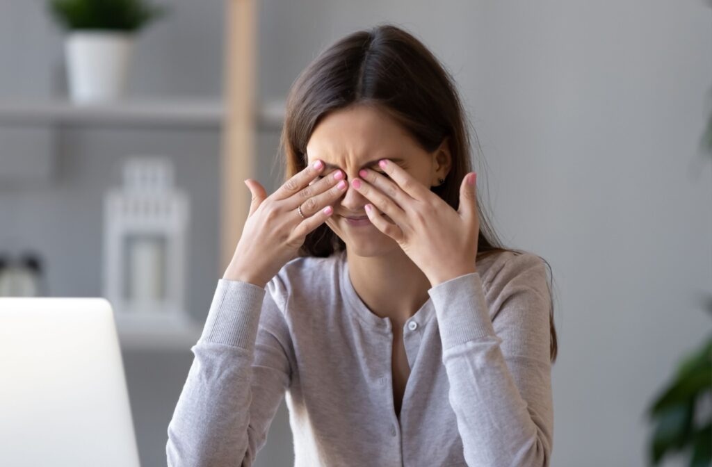 A person sits at a desk and rubs both eyes with their hands, showing signs of discomfort.