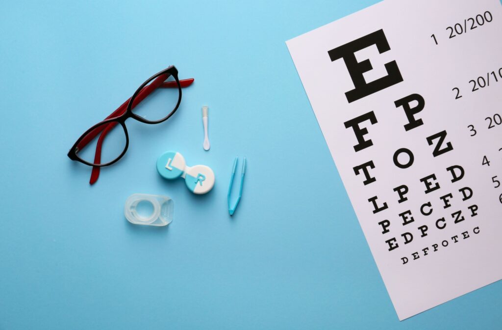 A pair of glasses and contact lenses beside an eye chart.