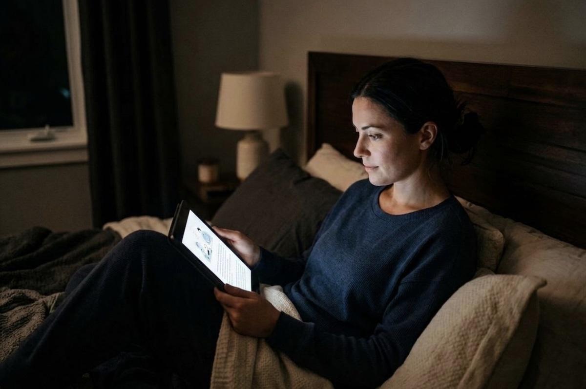 A person reading a tablet in bed in dim lighting.